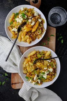 two white bowls filled with food on top of a wooden cutting board