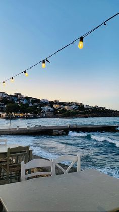 an outdoor dining area overlooking the ocean with lights strung from it's poles and chairs