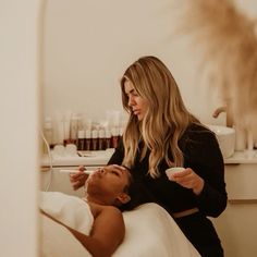 a woman is getting her hair done in the mirror while another woman brushes her teeth