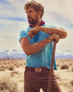 a man standing in the desert with his arms crossed and holding a wooden stick over his shoulder