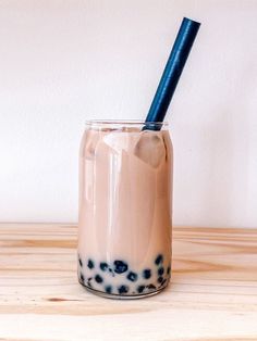 a glass with a straw in it sitting on a wooden table next to a white wall