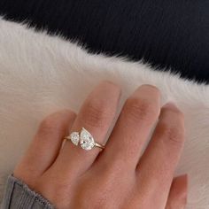 a woman's hand wearing a gold ring with two pear shaped diamonds on it