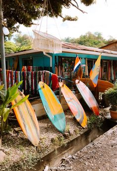 many surfboards are lined up in front of a building with clothes hanging from it