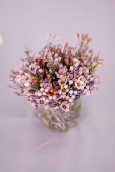 a small glass vase filled with lots of purple flowers on top of a white table