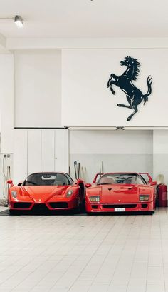 two red sports cars parked next to each other in front of a logo on the wall