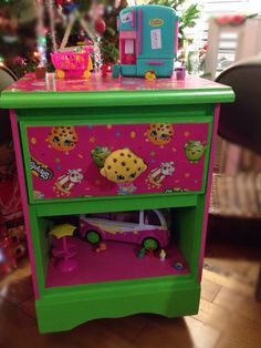 a green and pink toy dresser with toys on it's shelf next to a christmas tree