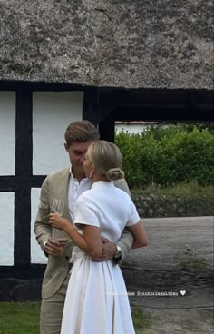 a man and woman standing next to each other in front of a thatched building