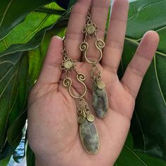 a person is holding some kind of earrings in their hand, with green leaves behind them