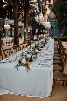 a long table is set up with white linens and greenery for an elegant dinner