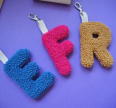 three crocheted key fobs sitting on top of a purple table next to a pencil