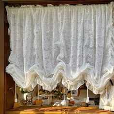 an open window with white lace curtains hanging from it's sides and shelves below