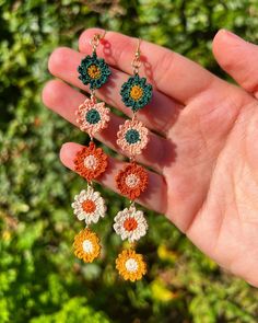 a hand holding four crochet flower earrings in it's left hand,