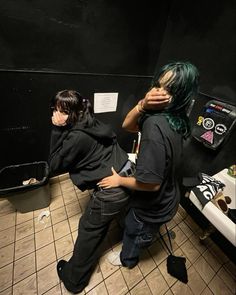 two people sitting in a bathroom with their backs to each other and one person covering his face