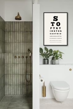 a white toilet sitting next to a walk in shower under a framed eye test chart