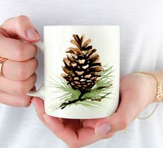 a person holding a coffee mug with a pine cone on it's front and side