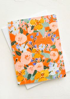 an orange and blue floral card on top of a white envelope