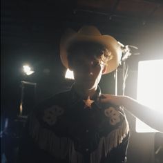 a man wearing a cowboy hat and holding his hand out to the light from behind him