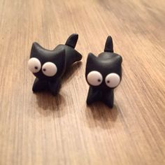 two black cat shaped earrings sitting on top of a wooden table