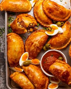 several pastries are arranged on a baking sheet with sauce and olives in the middle