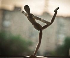 a wooden figurine is posed in front of a window