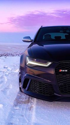 the front end of a black sports car parked on snow covered ground with purple sky in background