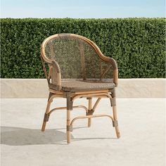 a wicker chair sitting on top of a cement floor next to a green hedge