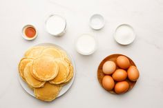 pancakes and eggs on a white plate next to bowls of milk, orange juice and other ingredients