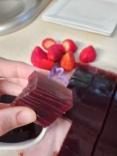 a person holding a piece of chocolate in front of some strawberries on the counter