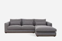 a gray sectional sofa with pillows on the top and bottom, sitting in front of a white background