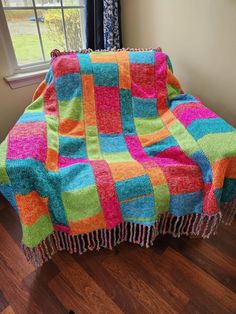 a multicolored blanket sitting on top of a wooden floor next to a window