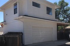 a car parked in front of a white two story house with a garage on the second floor