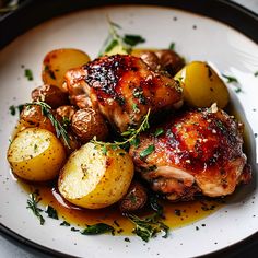 a white plate topped with chicken, potatoes and green garnish on top of a table