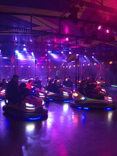 several people are riding bumper cars in an indoor area with lights on the ceiling and floor