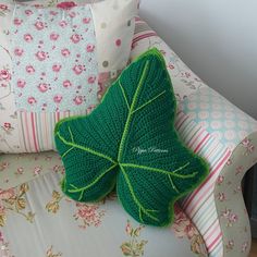 a crocheted green leaf pillow sitting on top of a white couch next to pillows