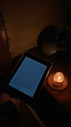 a tablet computer sitting on top of a wooden table next to a lit up candle