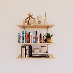 three wooden shelves with books, vases and other items on them against a white wall