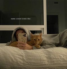 a woman laying in bed with an orange cat and taking a photo on her phone