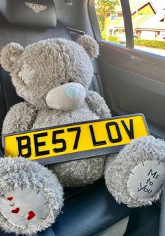 a teddy bear sitting in the back seat of a car holding a best loved sign