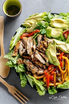 a salad with chicken, peppers and avocado on it next to a wooden spoon