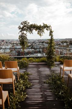 an outdoor seating area with wooden chairs and greenery on top of a building in the city