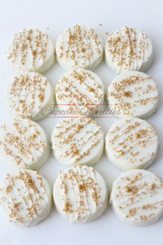 white frosted cupcakes with gold sprinkles are arranged on a white surface