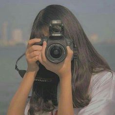 a woman holding up a camera to take a photo in front of the ocean with her hands