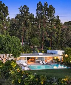 an aerial view of a house with a swimming pool in the foreground and trees surrounding it