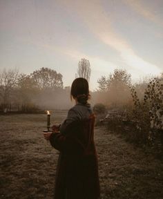 a woman holding a lit candle standing in a field