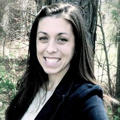 a woman standing in front of a tree smiling for the camera while wearing a black jacket