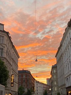 the sky is pink and orange as people walk down the street in front of buildings