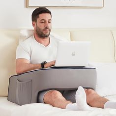 a man sitting on a bed with his laptop in front of him while using the pillow