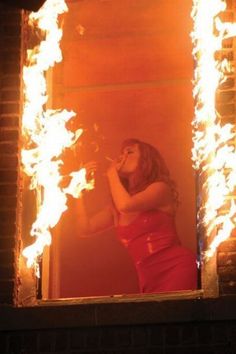 a woman standing in front of a mirror with fire coming out of it's sides