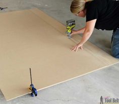 a woman is using a drill to paint a piece of cardboard on the floor with a screwdriver