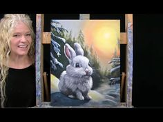 a woman standing in front of an easel holding up a painting with a rabbit on it